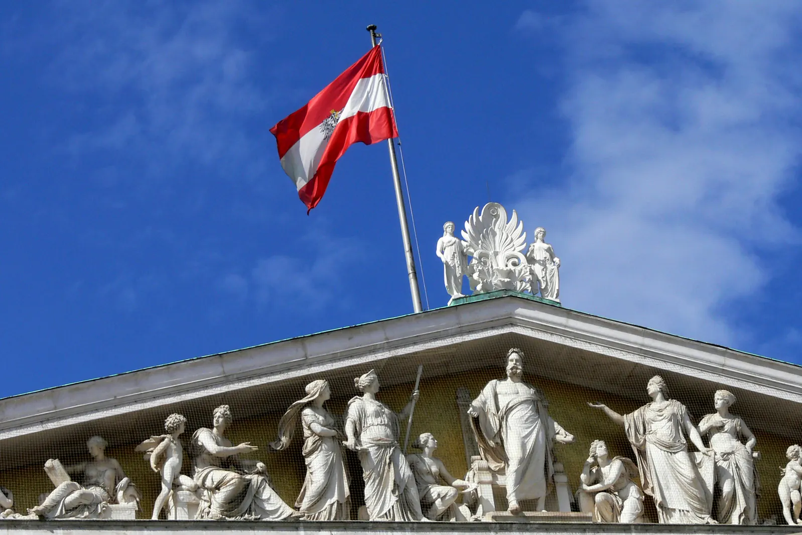 Rot-weiß-rote Fahne an einem Mast über dem Giebel des Parlaments mit Figuren