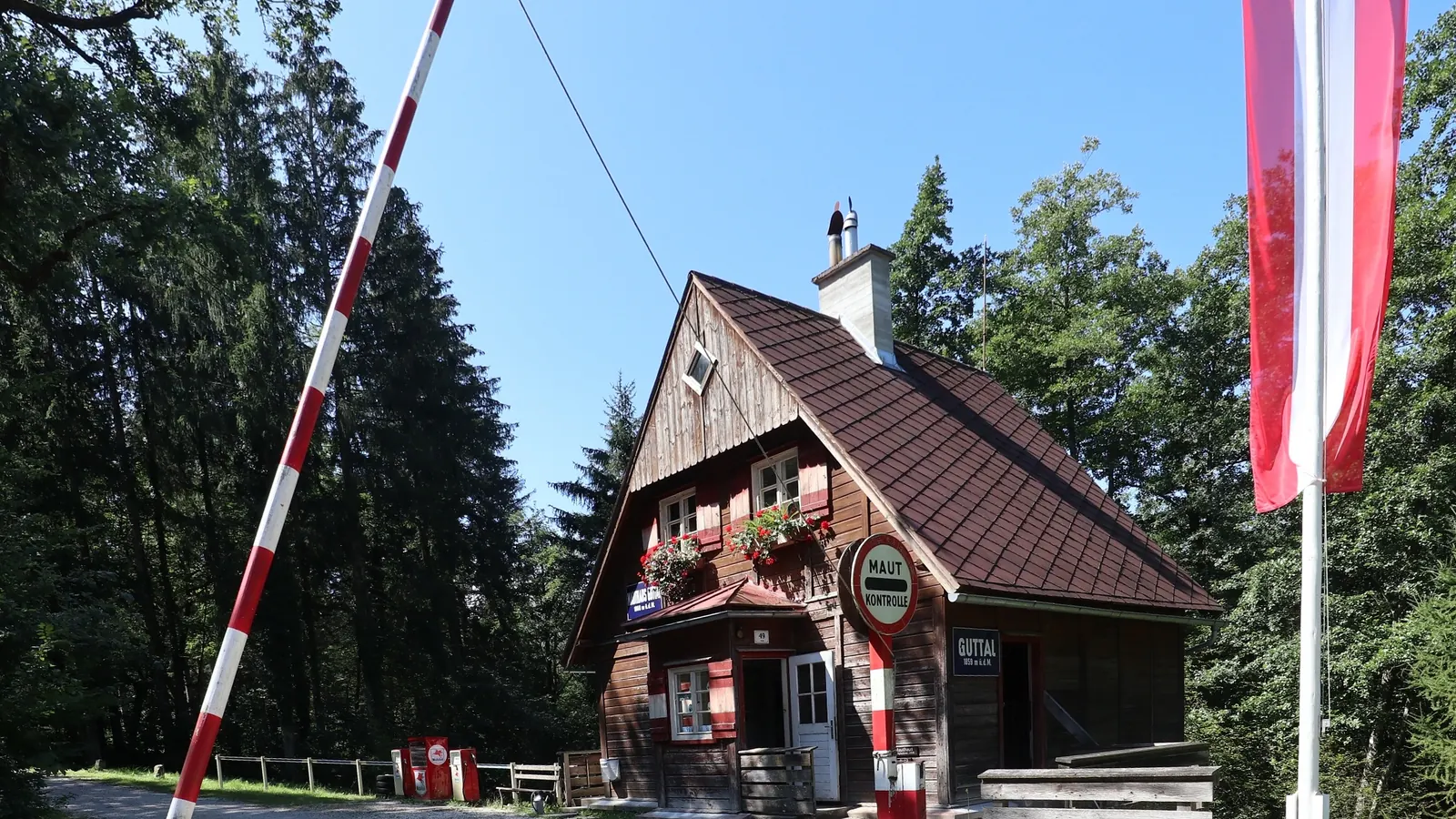 Altes Mauthaus mit rot-weißem Schlagbaum und einer rot-weiß-roten Fahne an einem Mast