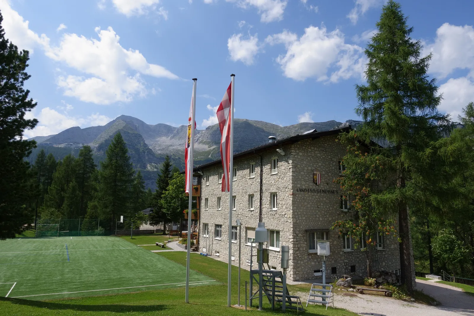 Zwei Fahnenmasten vor einem Steinhaus auf der Wurzeralm, dahinter Berge