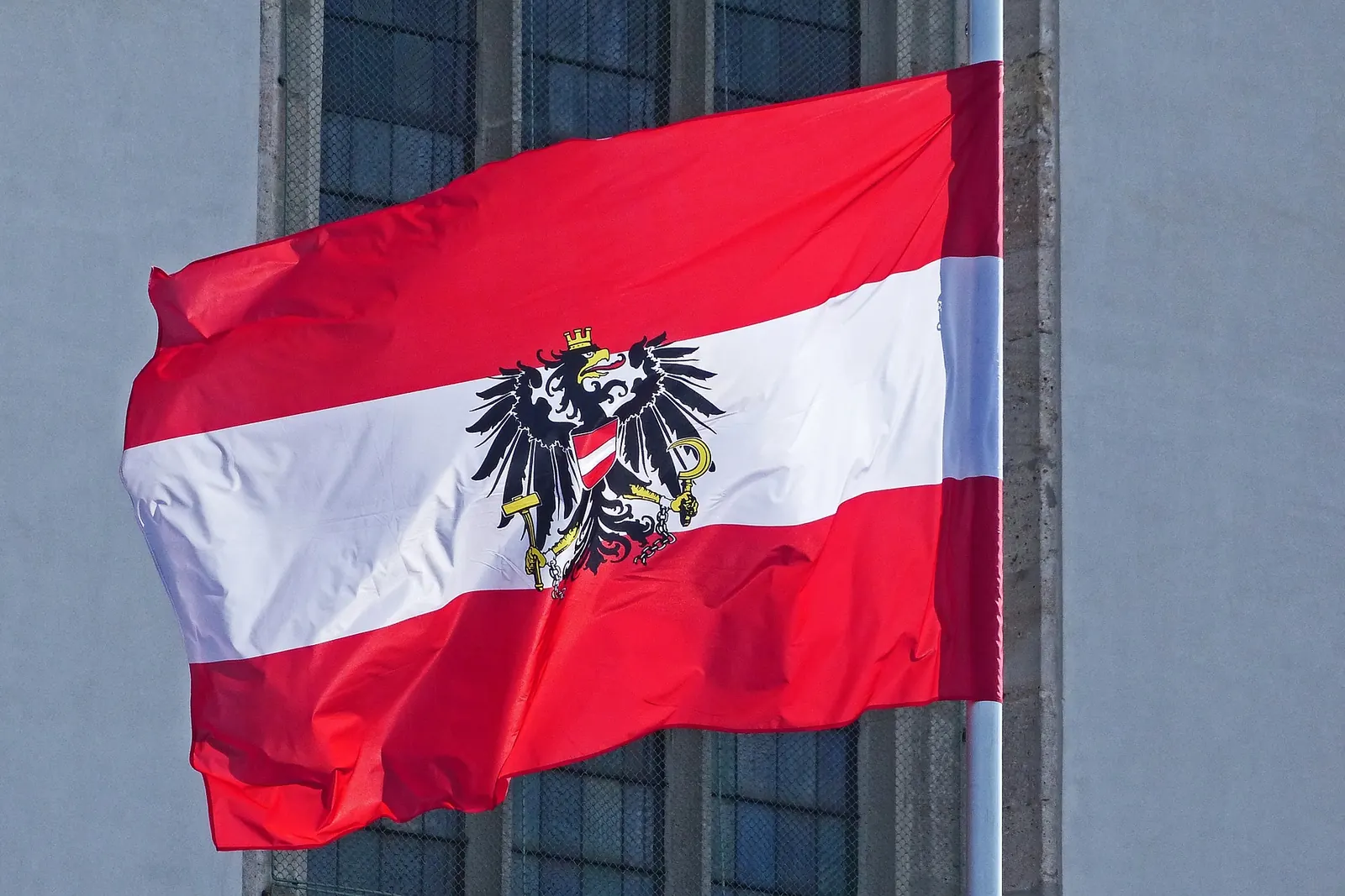 Die rot-weiß-rote Dienstflagge mit dem Bundeswappen an einem Mast vor einer Fassade