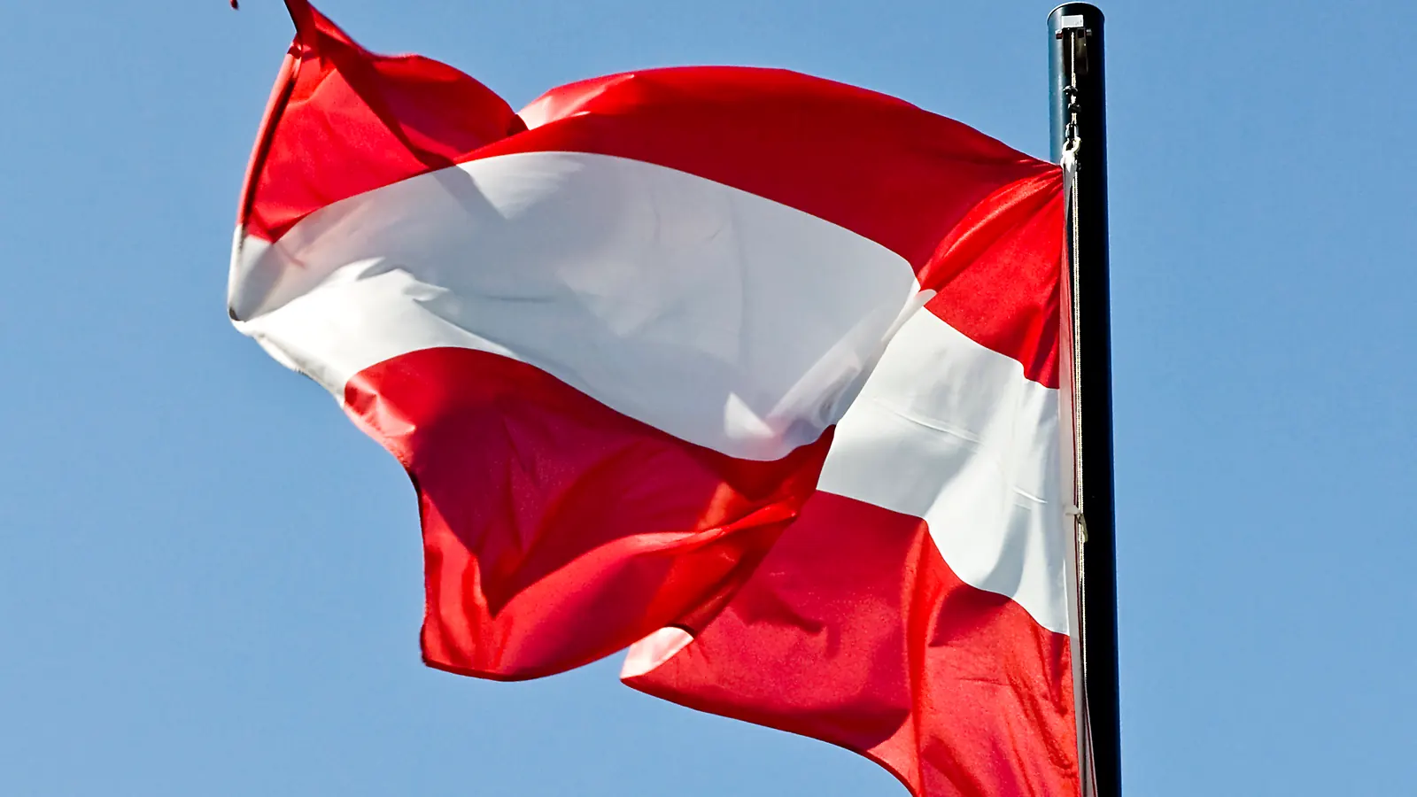 Die rot-weiß-rote Fahne Österreichs weht an einem Mast vor blauem Himmel