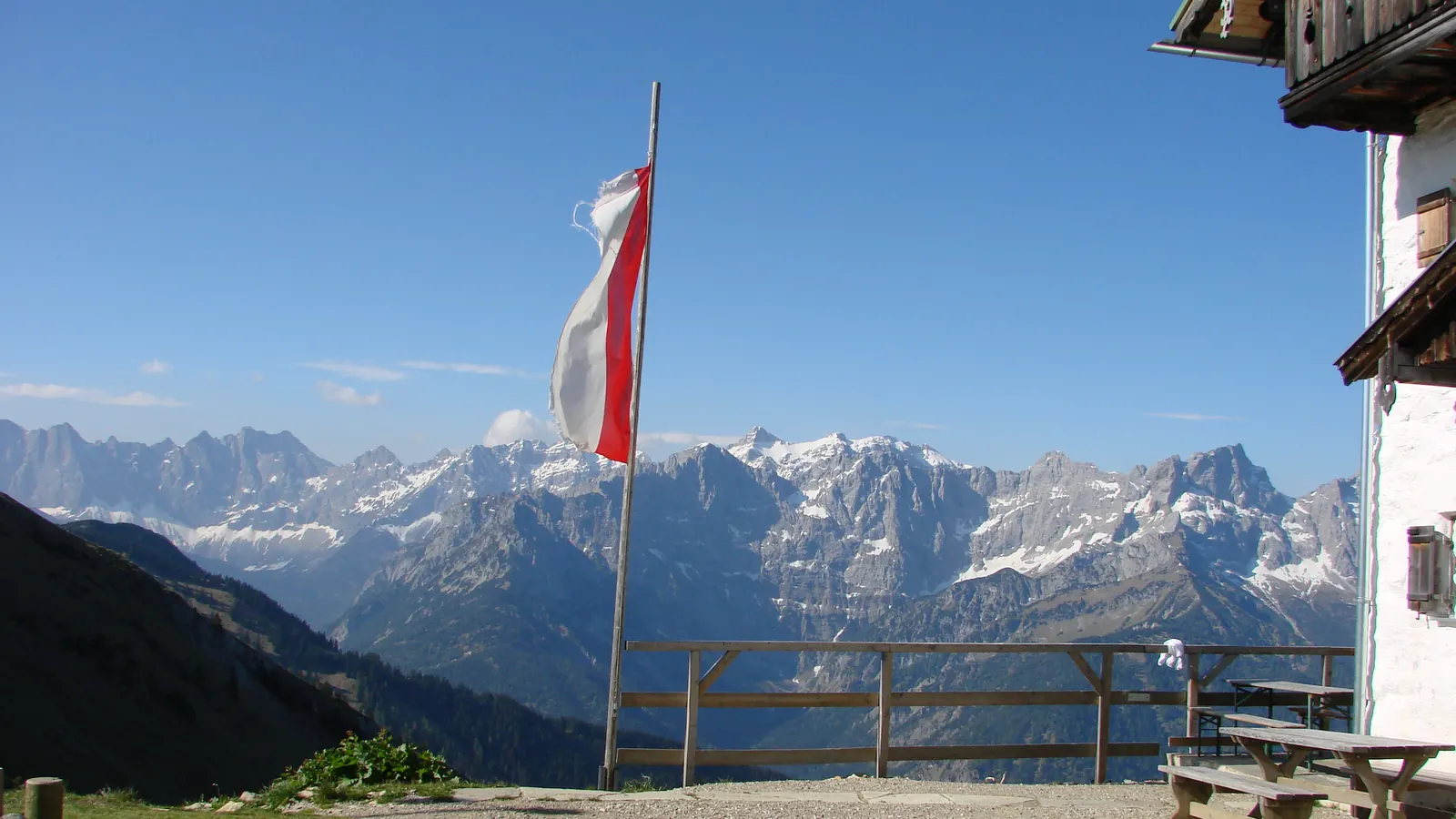 Rot-weiß-rote Fahne an einem Mast vor der Tölzer Hütte, dahinter die Gipfel des Karwendels