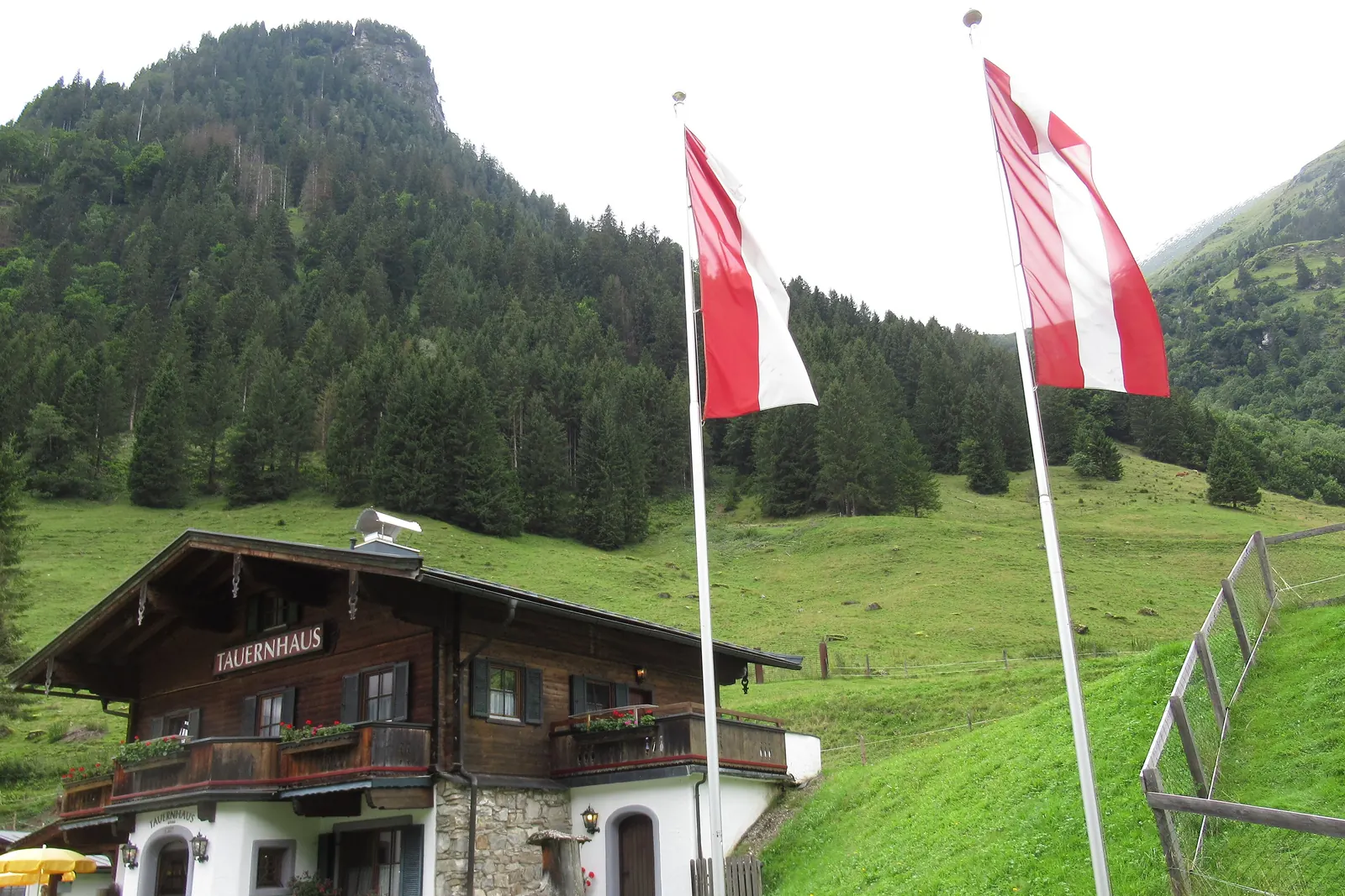 Das Tauernhaus Ferleiten mit der Salzburger Landesfahne und der Österreichfahne an zwei Masten vor bewaldeten Hängen