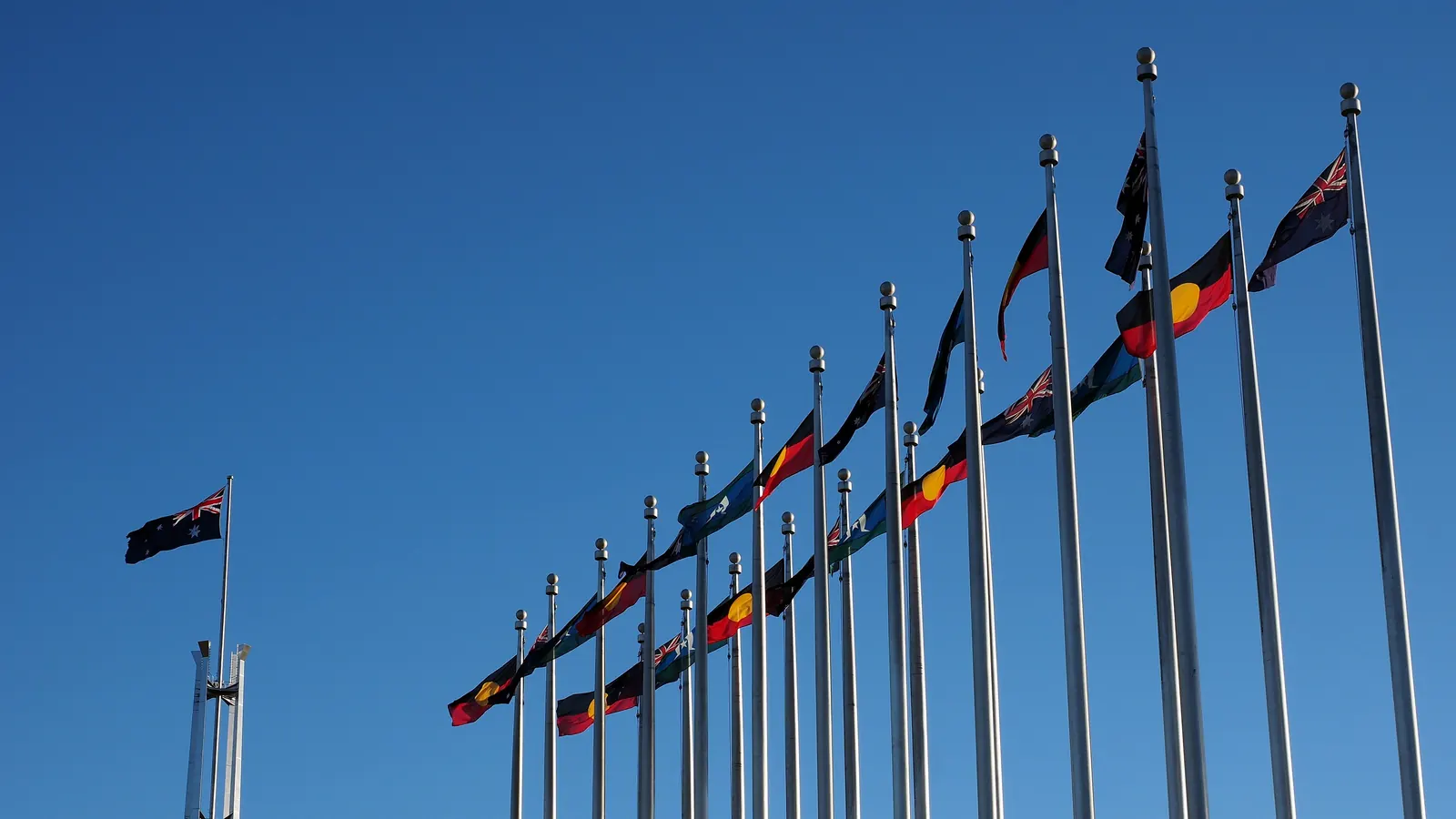 A row of flagpoles with the Australian National Flag, the Australian Aboriginal Flag and the Torres Strait Islander Flag outside Parliament House in Canberra