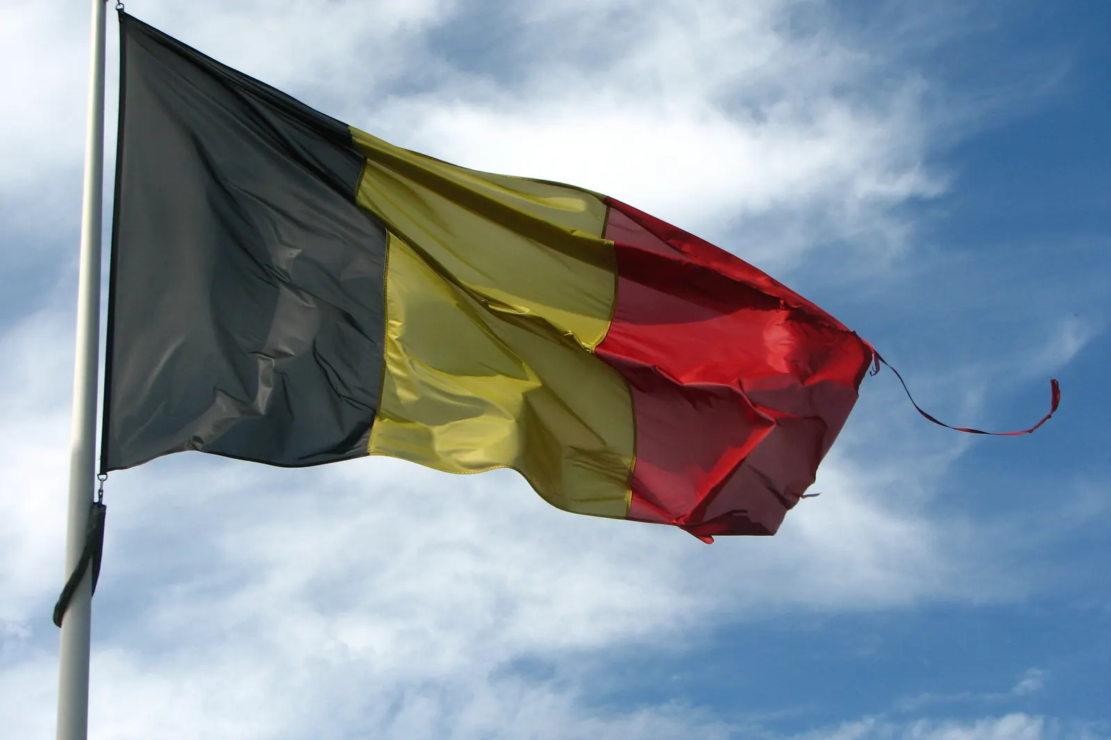 Een versleten Belgische vlag met rafels aan een mast in de wind