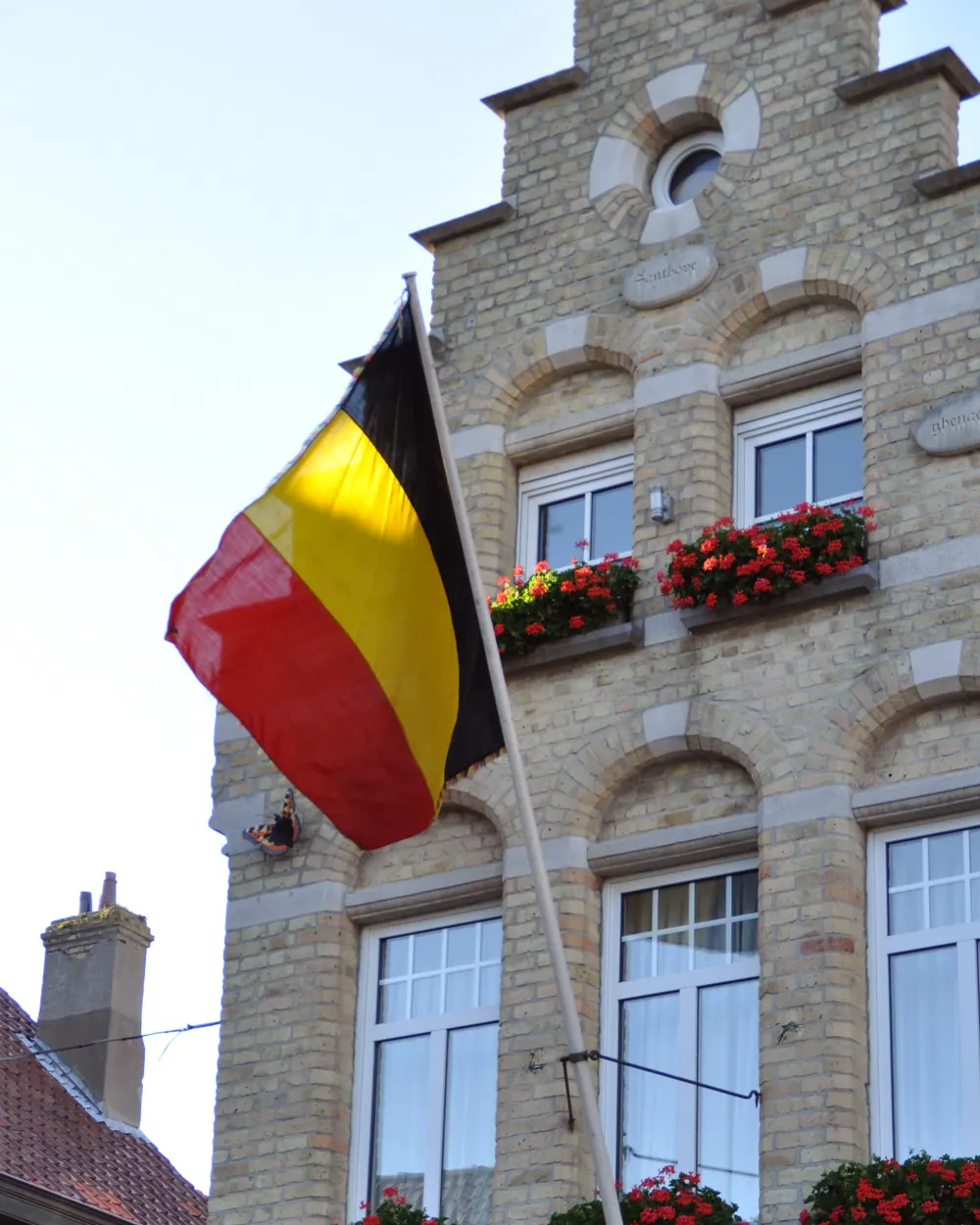 De Belgische vlag aan een stok aan de gevel van een huis met bloembakken