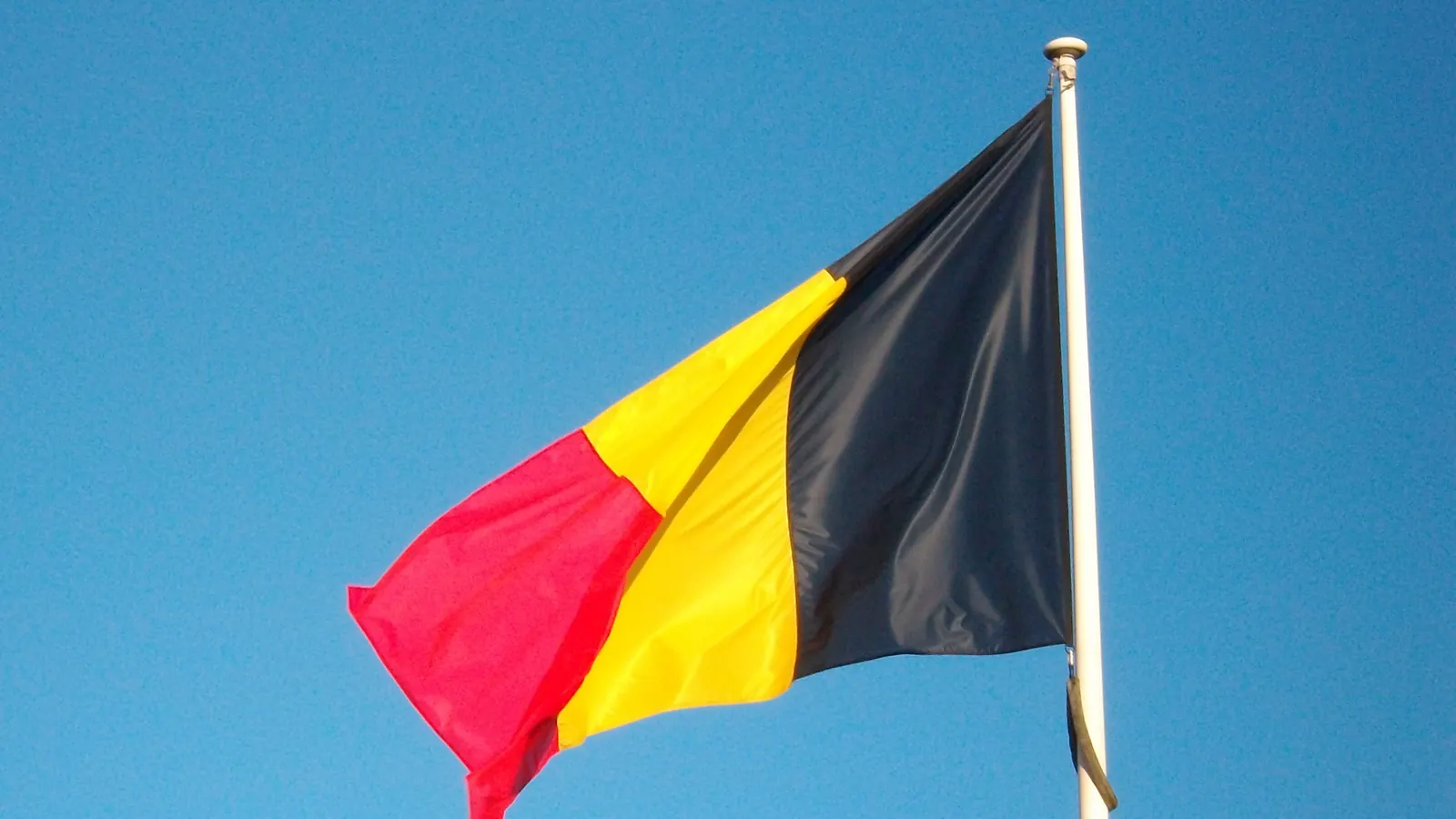 De Belgische driekleur in zwart, geel en rood aan een mast tegen een blauwe lucht