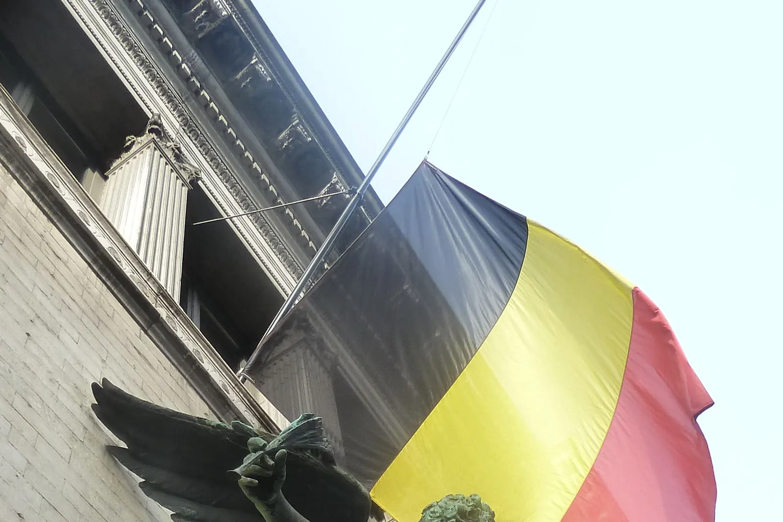 De Belgische vlag halfstok boven een bronzen beeld, bij de uitvaart van koningin Fabiola