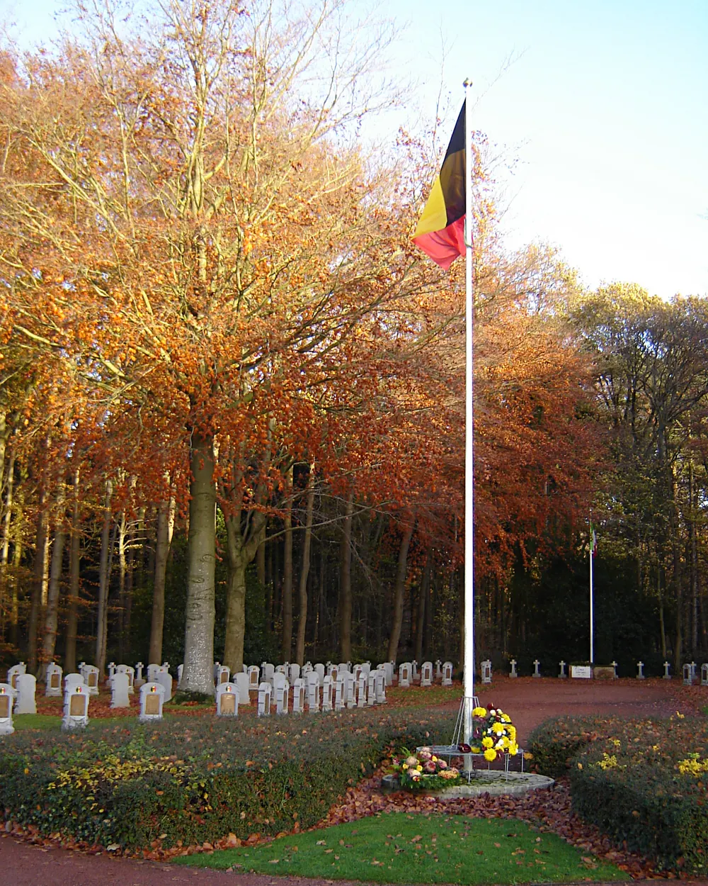 De Belgische vlag aan een hoge mast op de militaire begraafplaats van Houthulst in de herfst