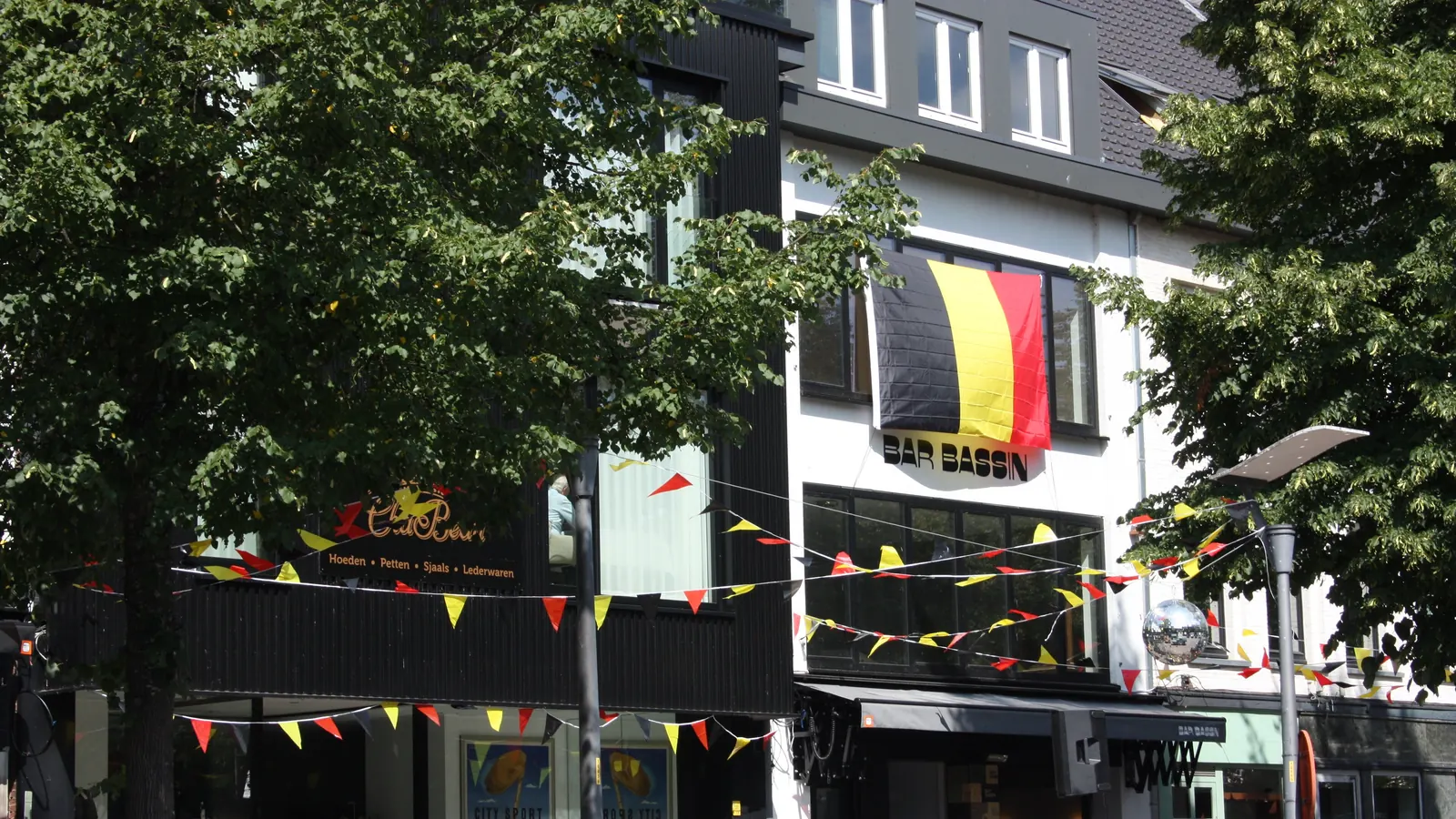 Een café in Genk met een grote Belgische vlag aan de gevel en vlaggetjes in zwart, geel en rood