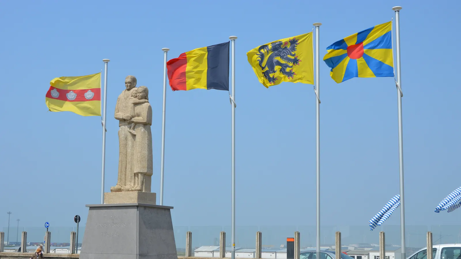 Het Vissersmonument in Heist met de vlaggen van Knokke-Heist, België, Vlaanderen en West-Vlaanderen