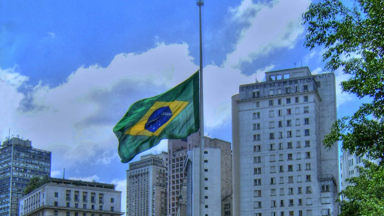 A Bandeira Nacional a meio-mastro diante de edifícios altos em São Paulo