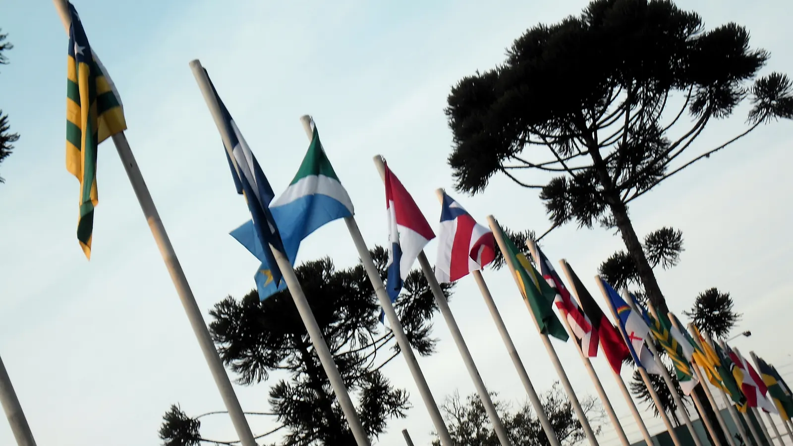 Bandeiras de vários países em uma fileira de mastros na Praça dos Migrantes, em Cascavel, Paraná