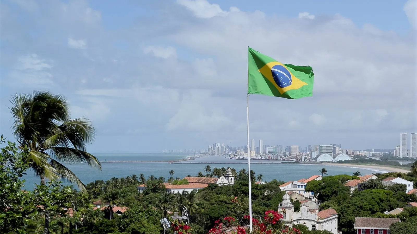 A Bandeira Nacional em um mastro sobre os telhados de Olinda, com Recife ao fundo