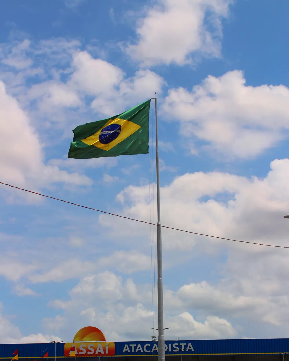 Um mastro alto com a Bandeira Nacional diante de uma loja atacadista