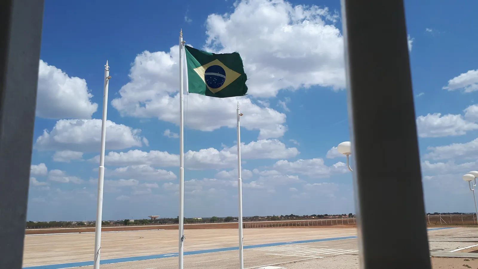 Três mastros com a Bandeira Nacional ao centro diante de um pátio aberto