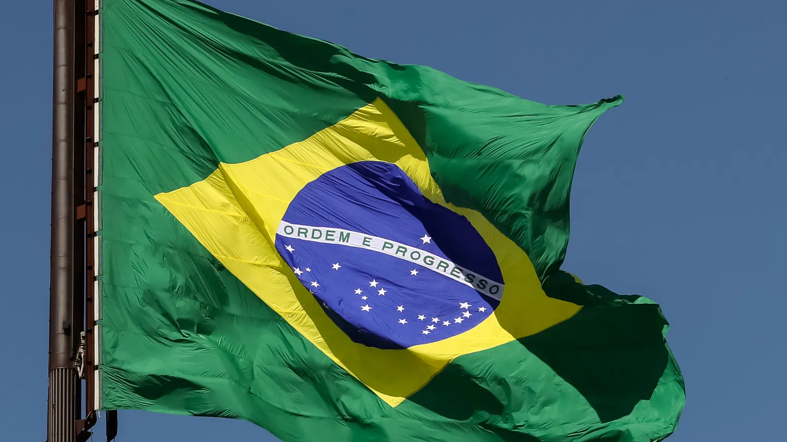 A Bandeira Nacional ao vento, com o círculo azul estrelado e a faixa Ordem e Progresso