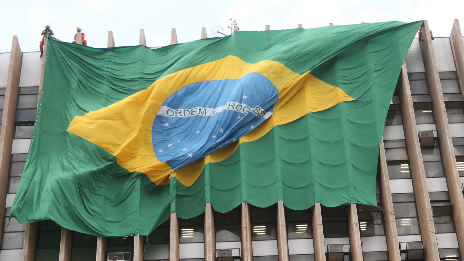 Bombeiros penduram uma bandeira gigante na fachada de um prédio anexo ao Palácio do Buriti, em Brasília