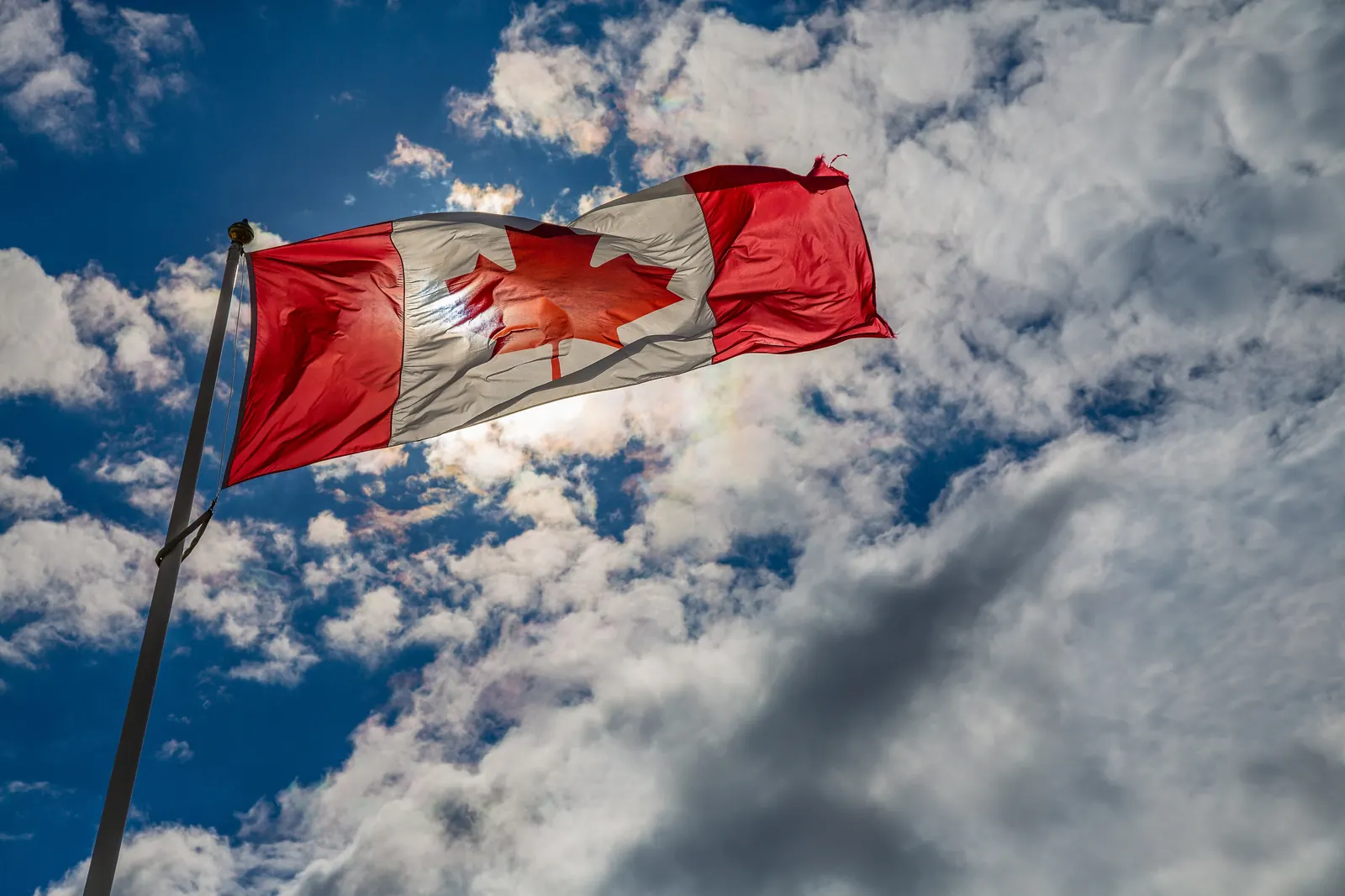 The flag of Canada on a flagpole against dramatic white clouds and a deep blue sky