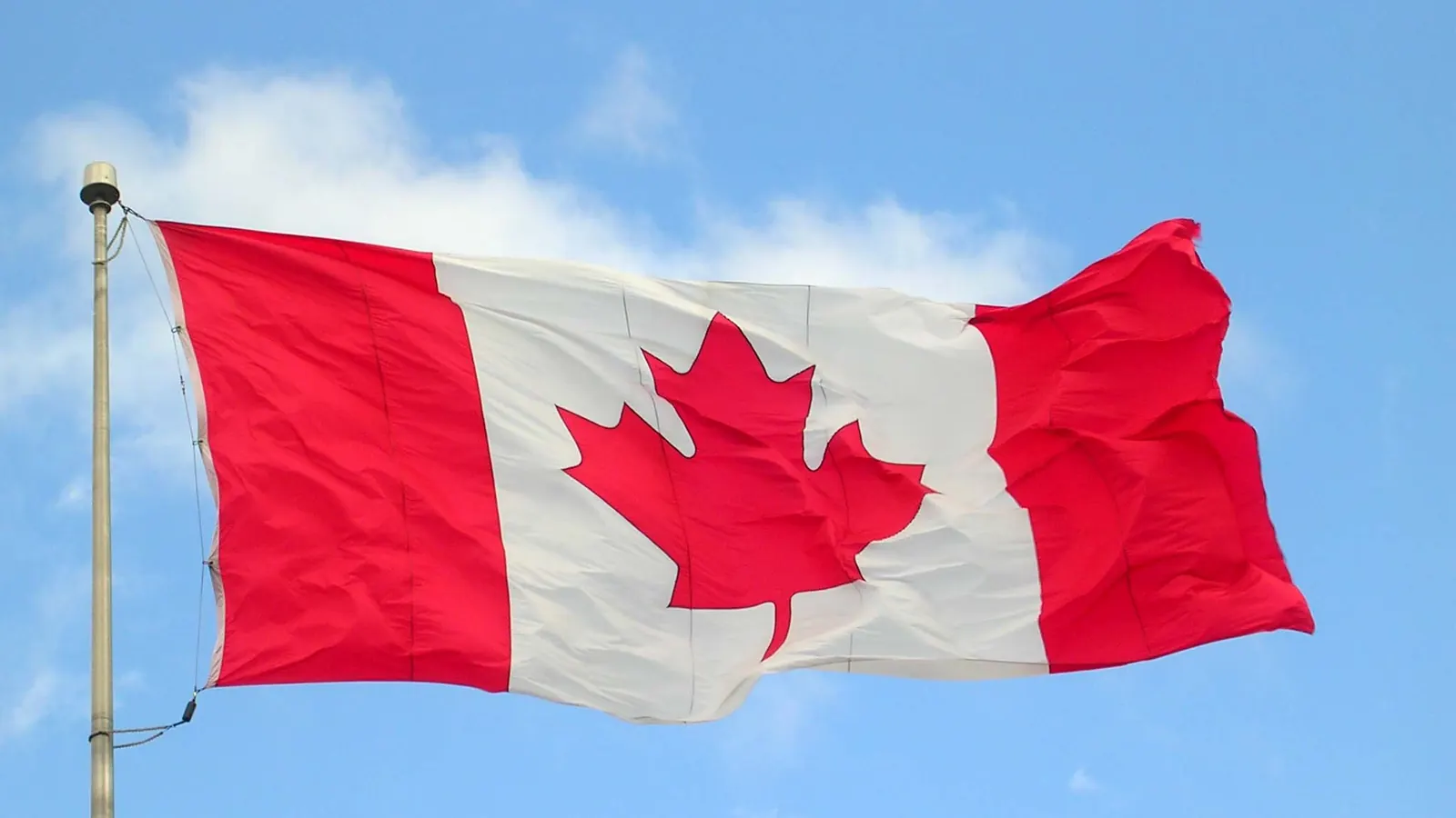 The red and white maple leaf flag flying from a flagpole against a blue sky in Halifax
