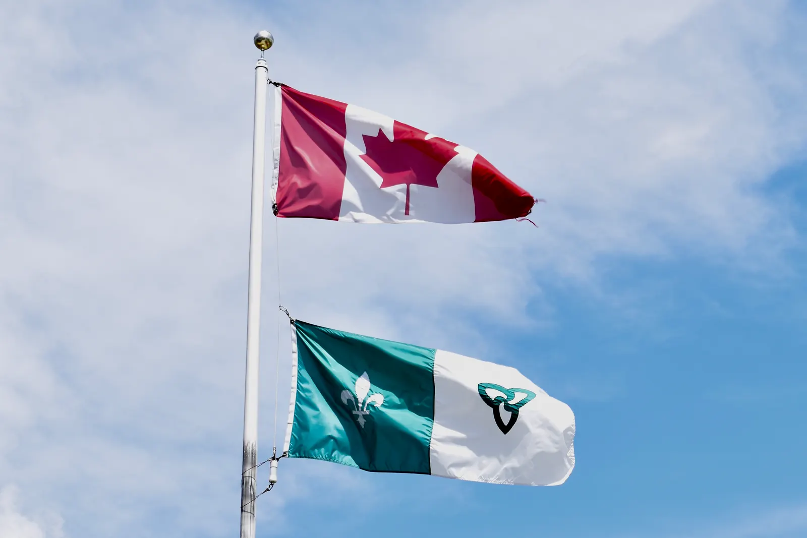 The flag of Canada above the green and white Franco-Ontarian flag on one flagpole in Sudbury
