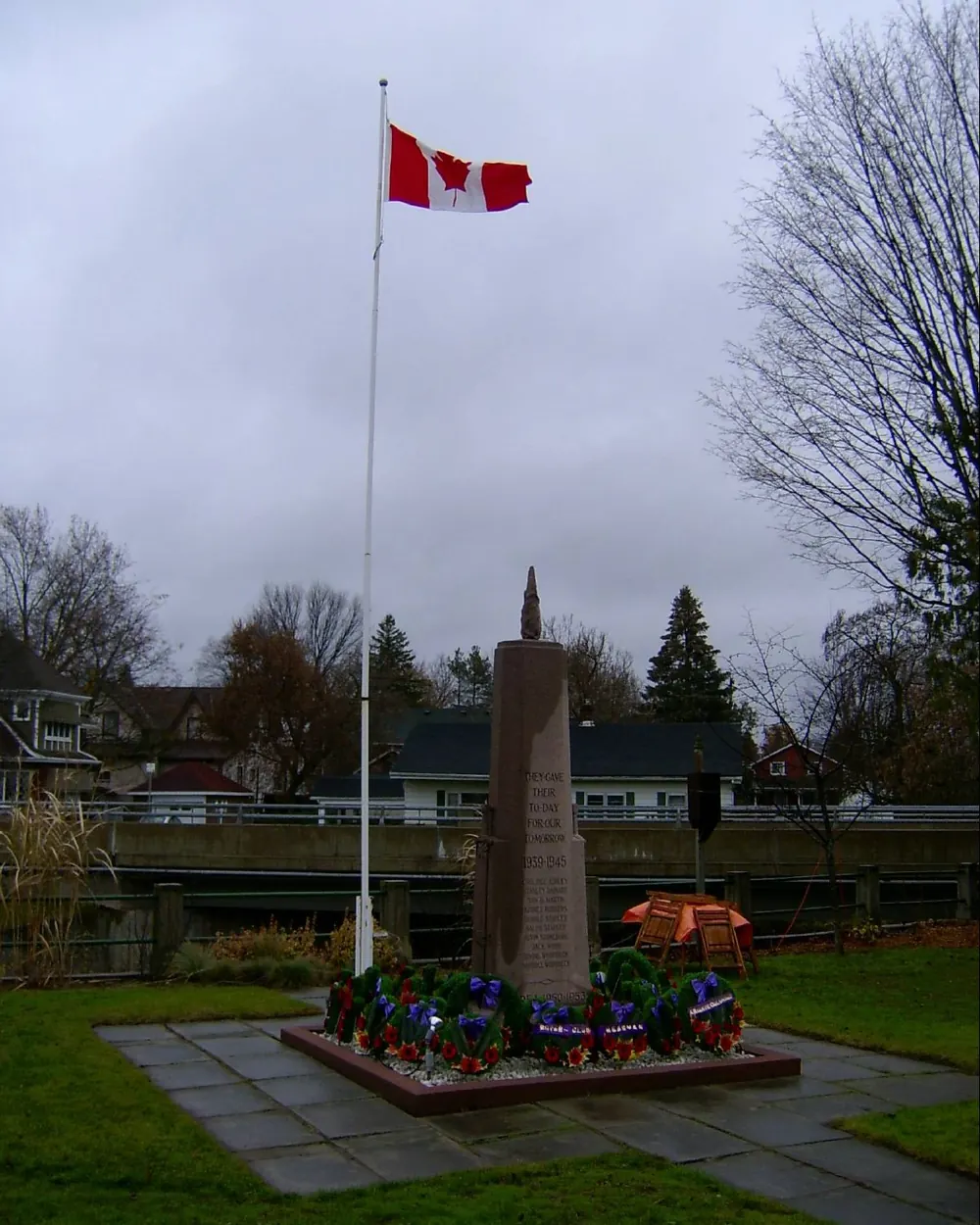 The flag of Canada on a flagpole above a war memorial with wreaths laid on Remembrance Day