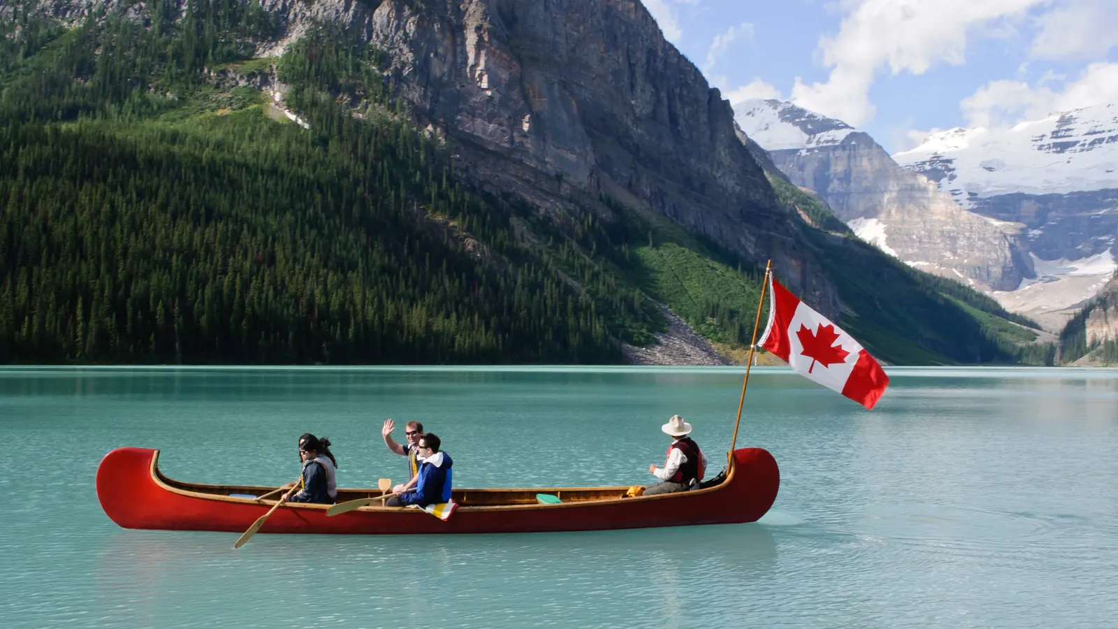 A red canoe flying the flag of Canada on the turquoise water of Lake Louise in Banff National Park, with mountains behind