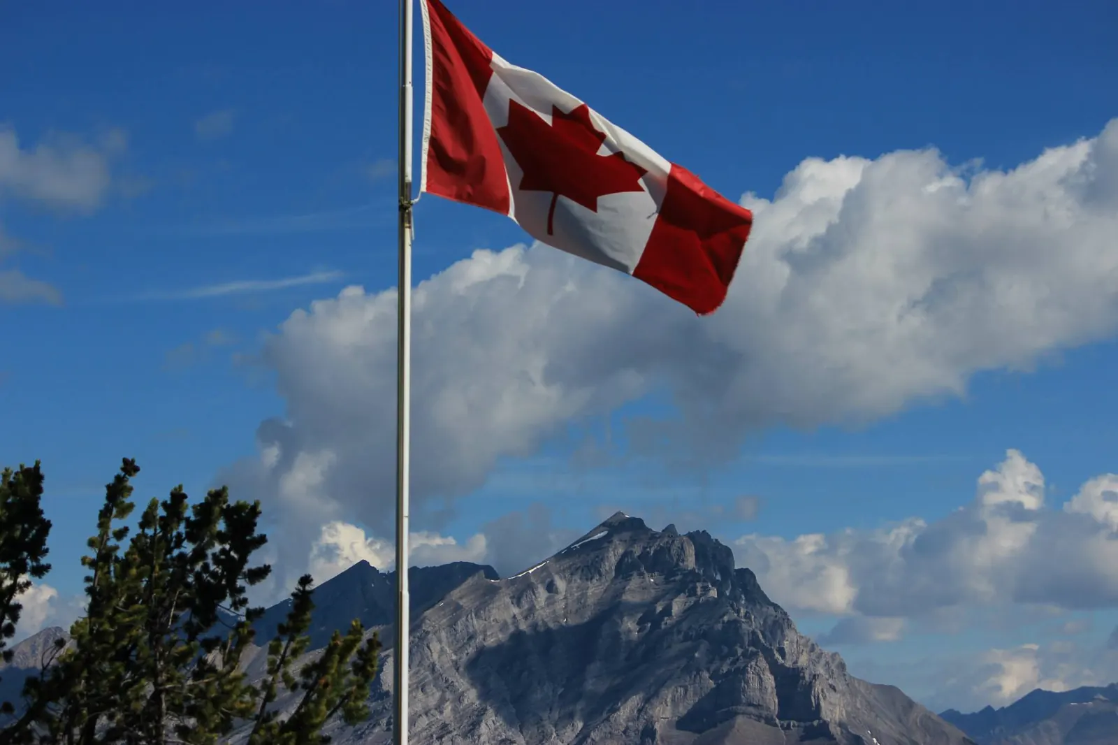 The flag of Canada on a flagpole in front of the mountains at Banff