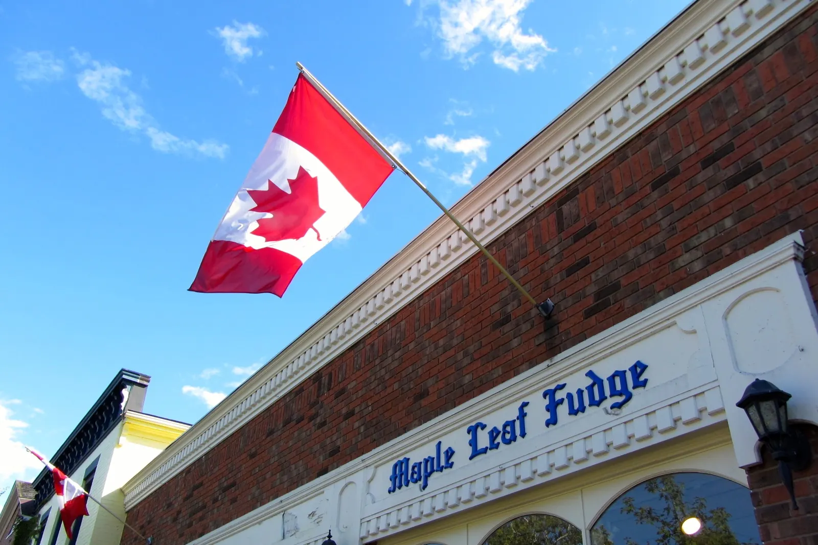 The flag of Canada on an angled pole from the brick front of a shop