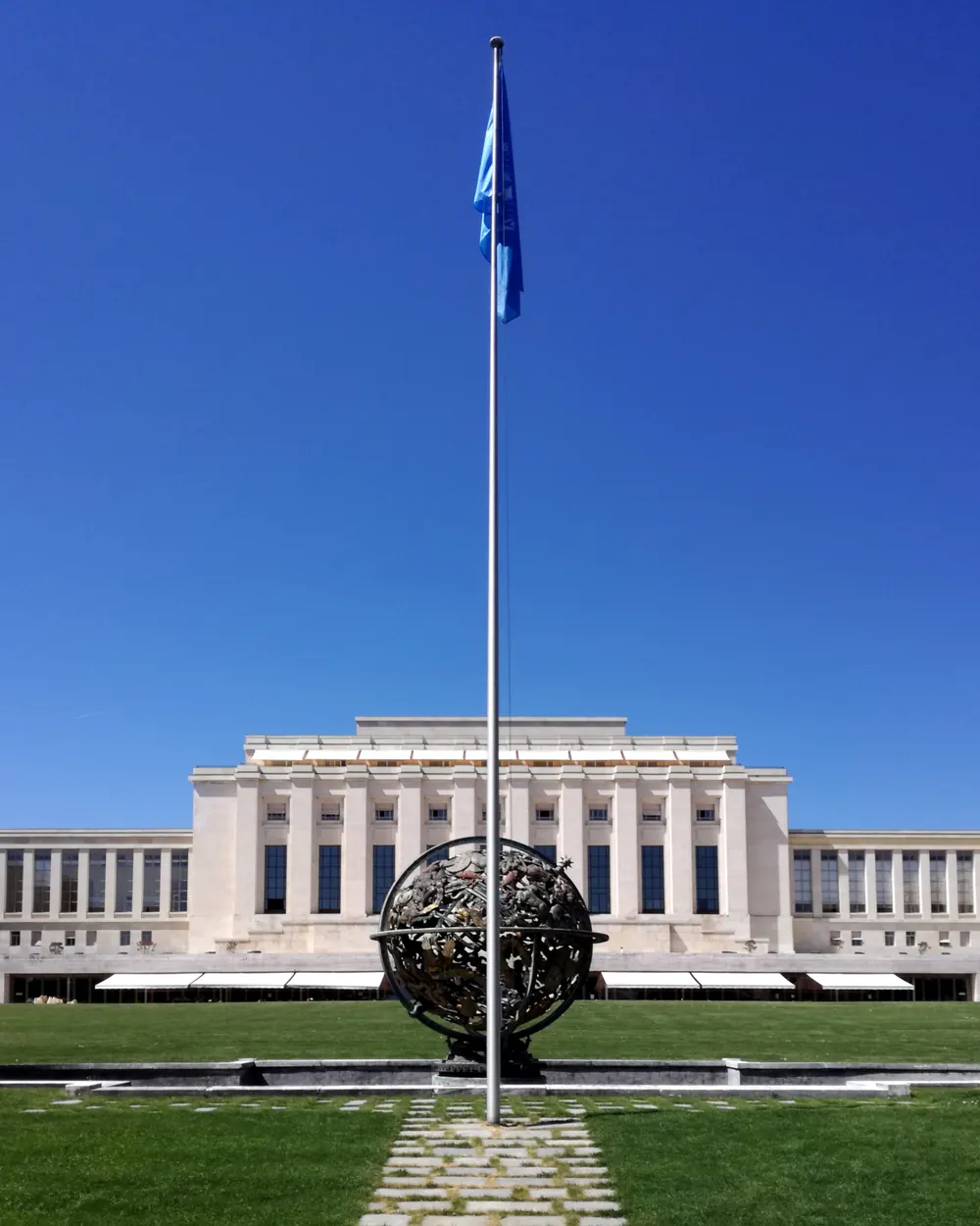 UNO-Fahne an einem hohen Mast hinter der Wilson-Kugel vor dem Palais des Nations