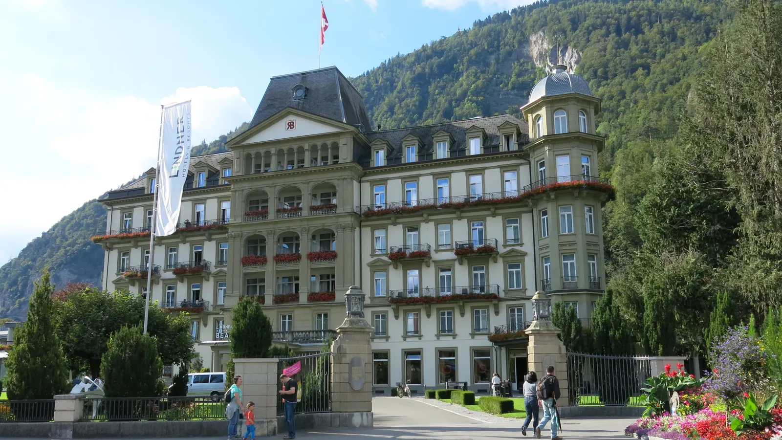 Das Hotel Beaurivage in Interlaken mit Fahnen an Masten vor den Bergen