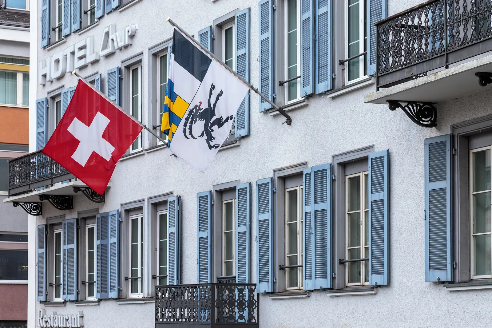 Schweizerfahne und Bündner Fahne an Auslegern an der Fassade des Hotels Chur