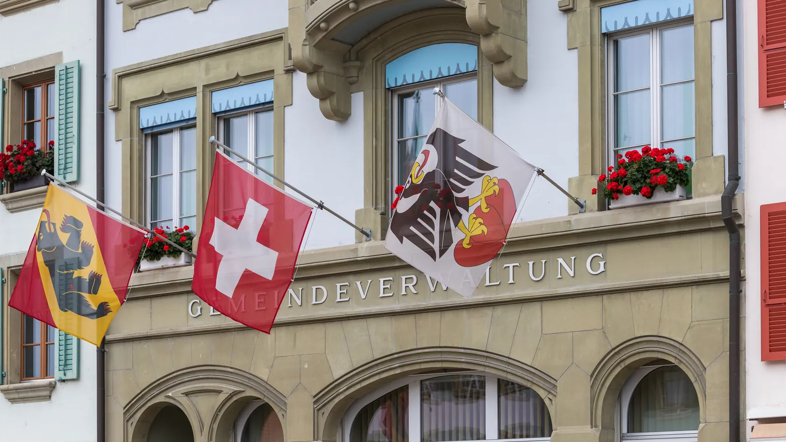 Gemeindeverwaltung Aarberg mit Berner Fahne, Schweizerfahne und Aarberger Fahne an der Fassade, die Schweizerfahne in der Mitte
