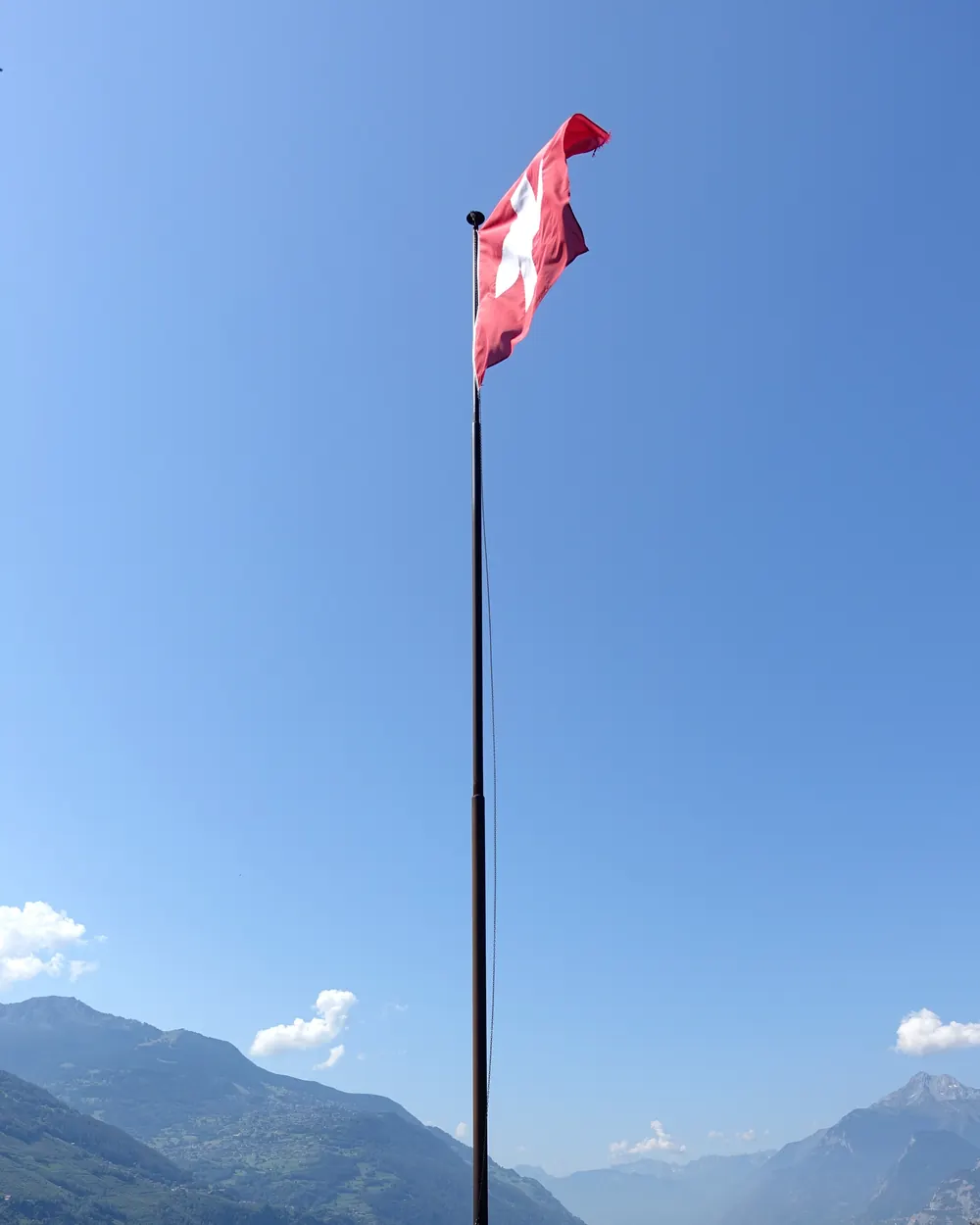 Schweizerfahne an einem hohen Mast über Sion, dahinter das Rhonetal