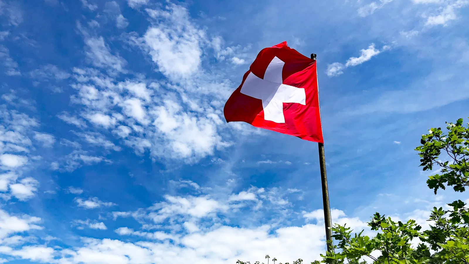 Schweizerfahne an einem Mast auf der Ravellenfluh vor blauem Himmel mit Wolken