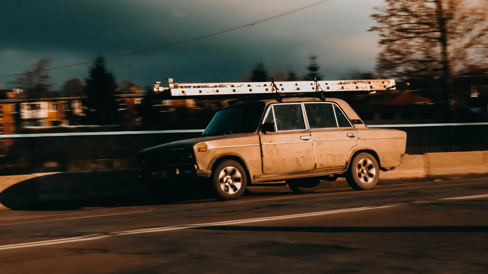 A car with a long ladder on the roof rack