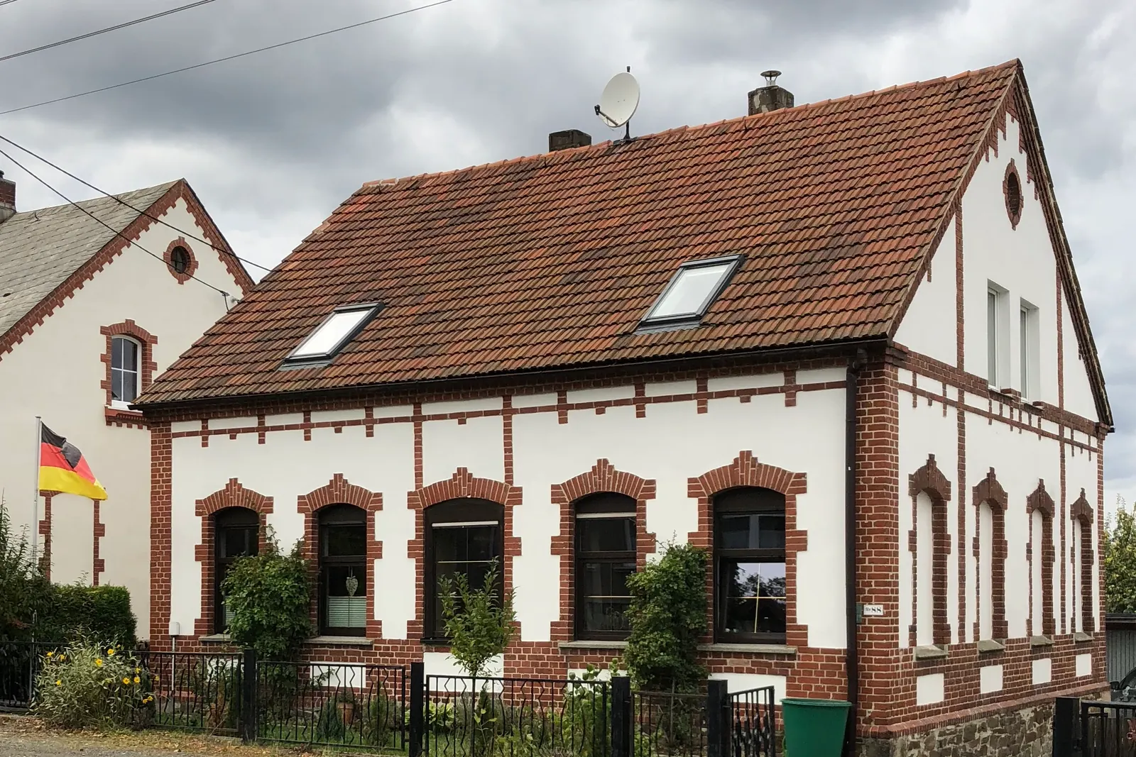 Backsteinhaus von 1900 mit einem kleinen Fahnenmast und Bundesflagge im Vorgarten