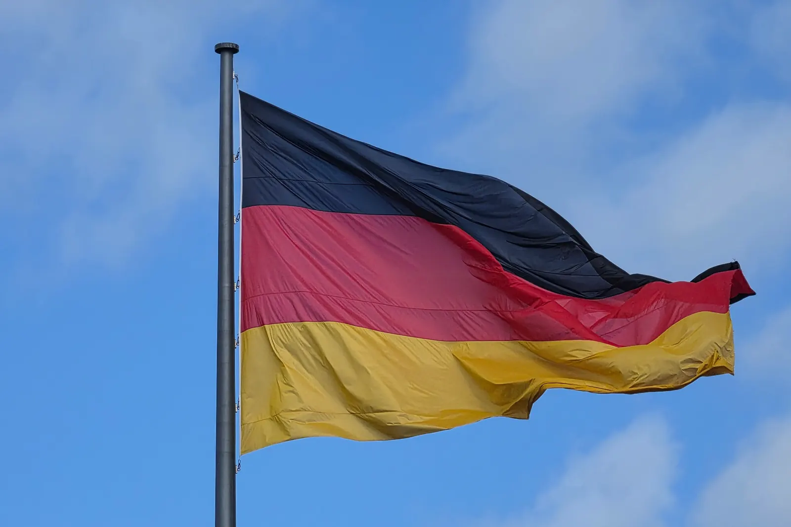 Die große Bundesflagge der Einheit vor dem Reichstagsgebäude vor blauem Himmel