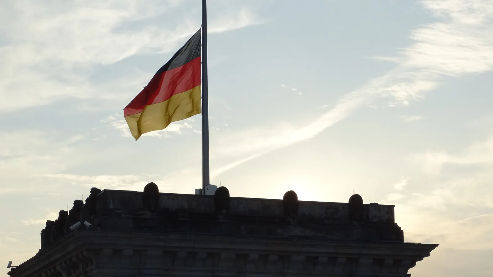 Bundesflagge auf halbmast auf einem Eckturm des Reichstagsgebäudes im Gegenlicht