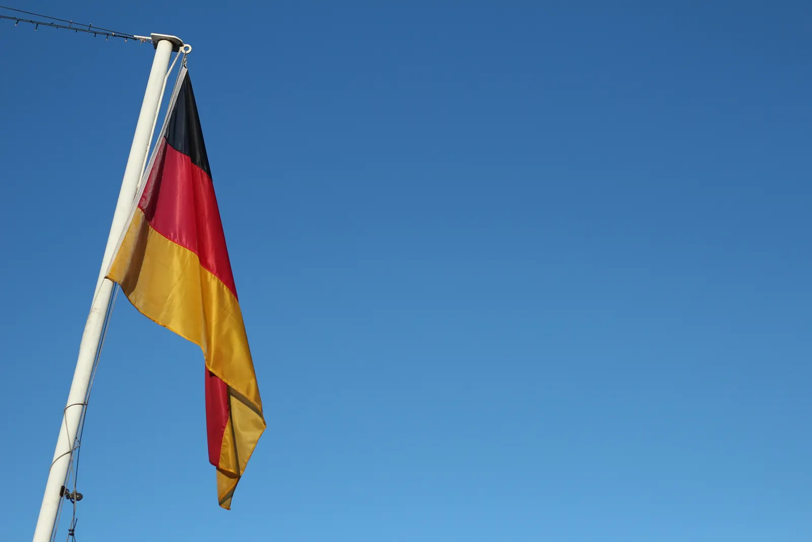Bundesflagge an einem weißen Fahnenmast vor blauem Himmel