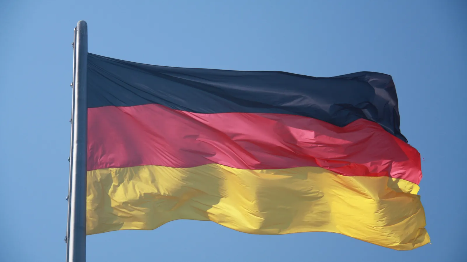 Die schwarz-rot-goldene Bundesflagge weht an einem Mast vor blauem Himmel