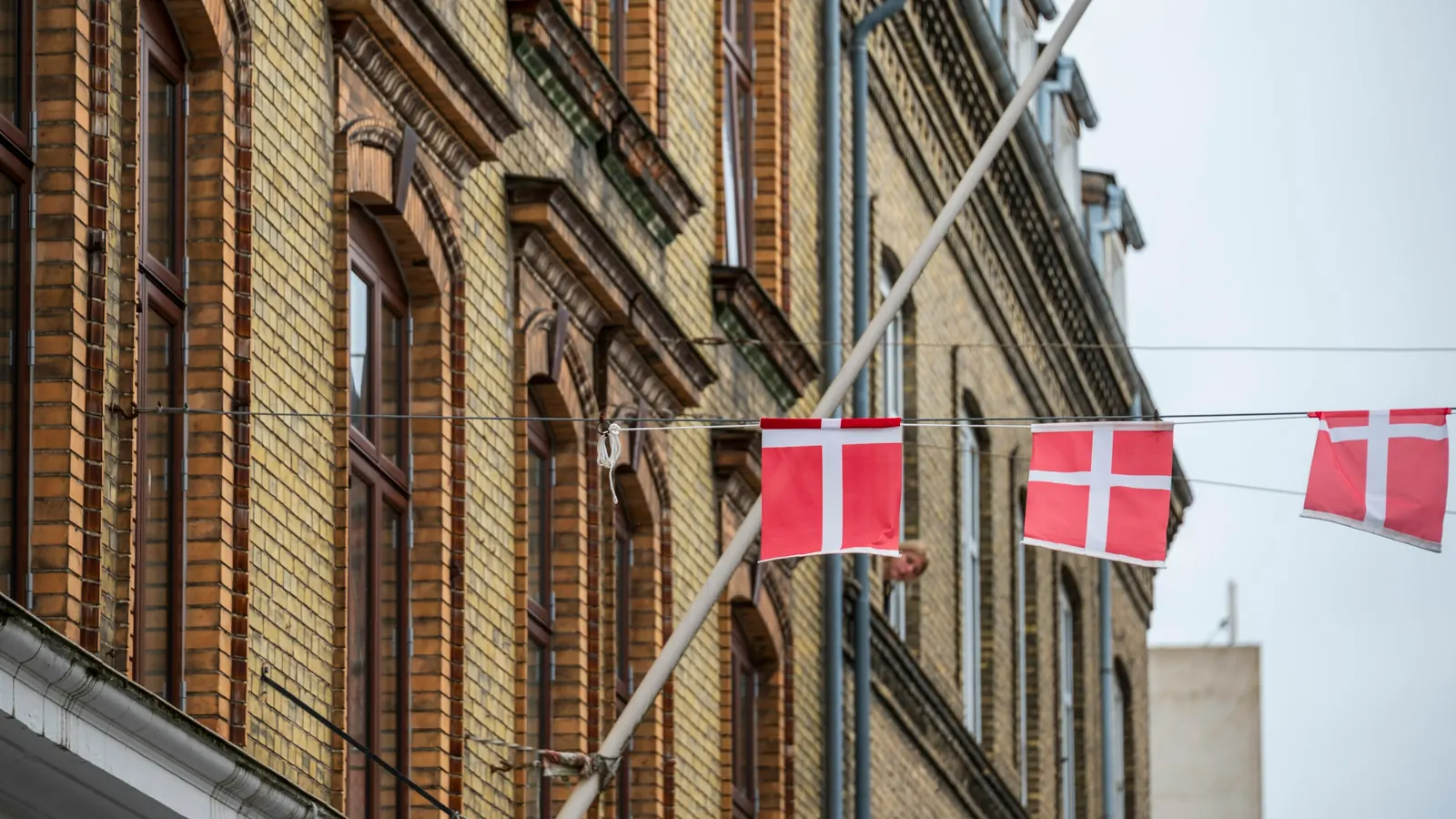 Skråtstillet flagstang på en murstensfacade og en guirlande med små dannebrogsflag over gaden