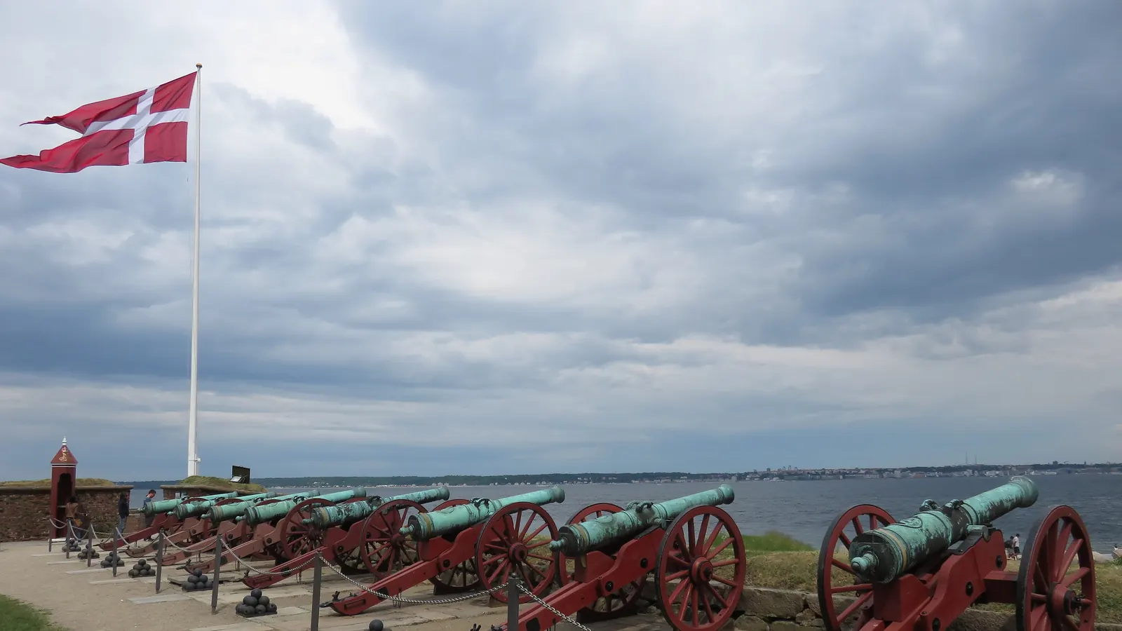 Splitflaget på en høj flagstang på Kronborgs flagbastion over en række gamle kanoner ud mod Øresund