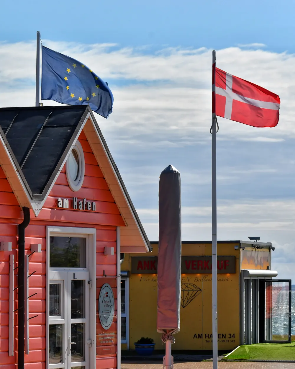 Dannebrog og EU-flaget på to flagstænger ved et rødt træhus