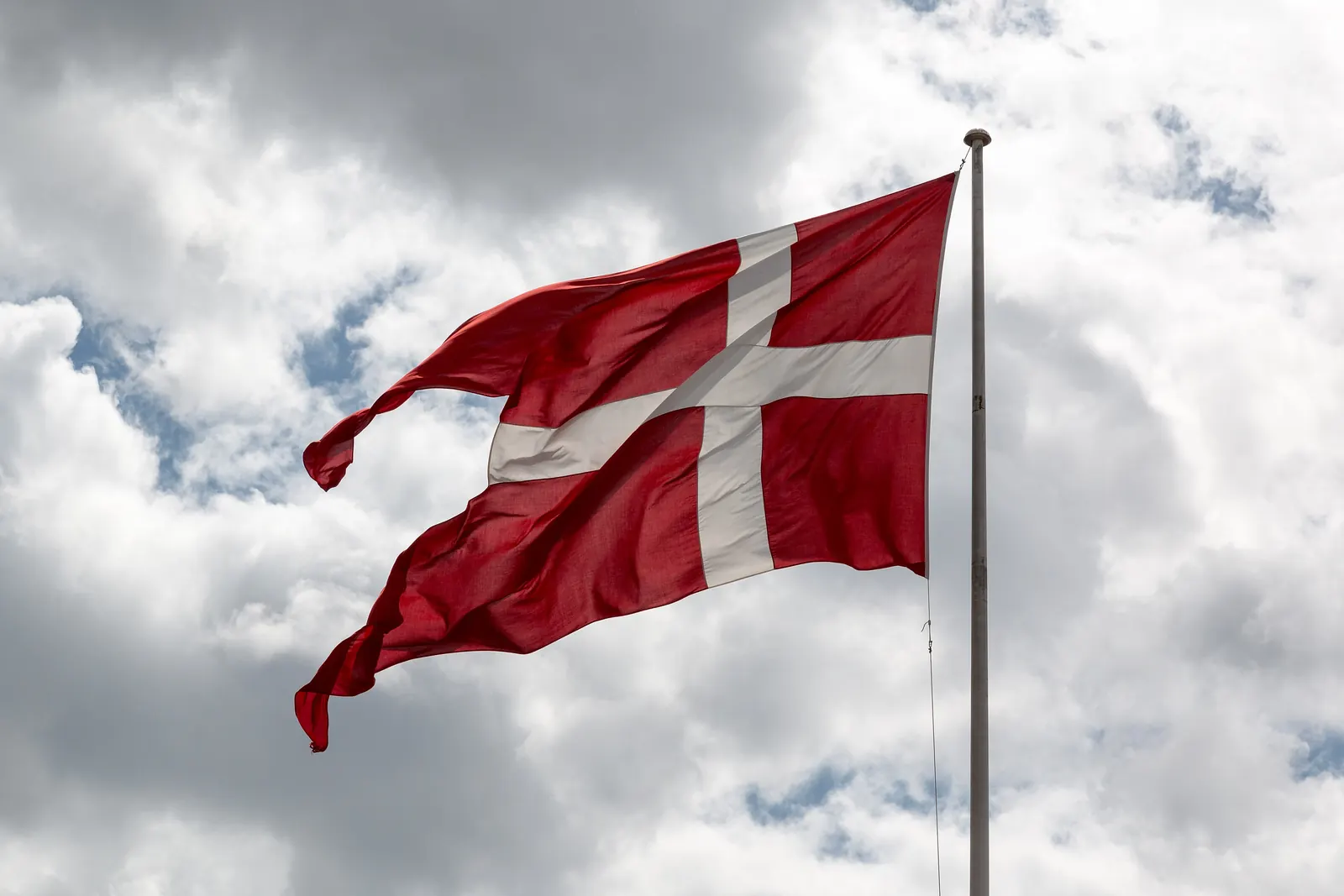 Dannebrog vajer på en flagstang mod en skyet himmel
