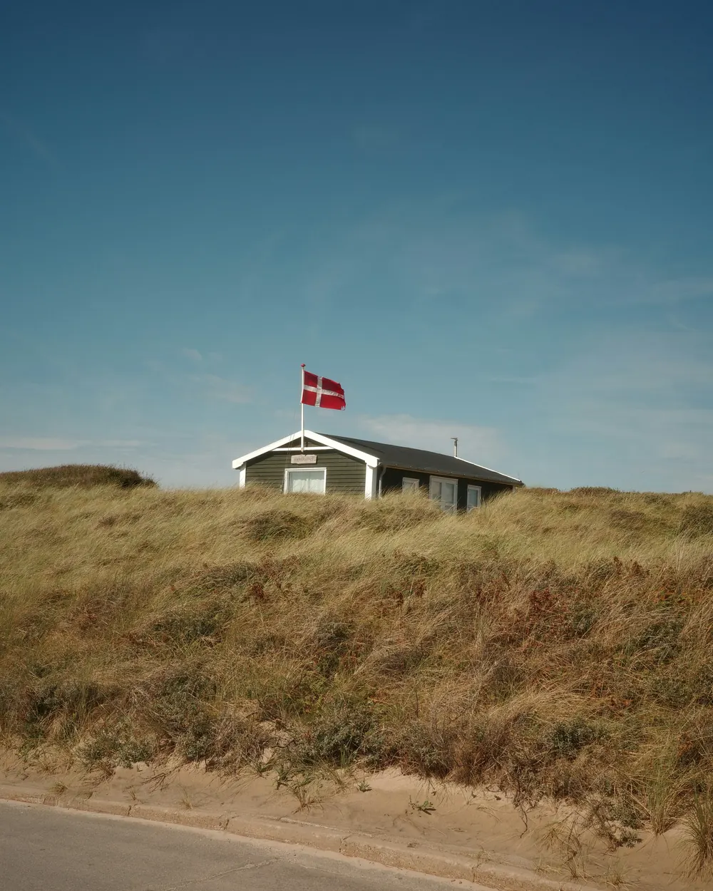 Lille sommerhus på toppen af en klit med Dannebrog på en flagstang