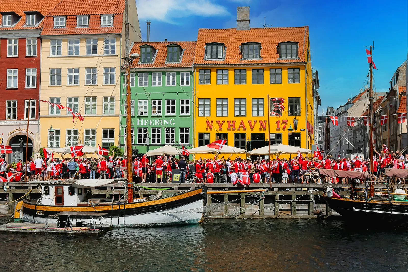 Nyhavn i København fyldt med mennesker og dannebrogsflag foran de farverige huse