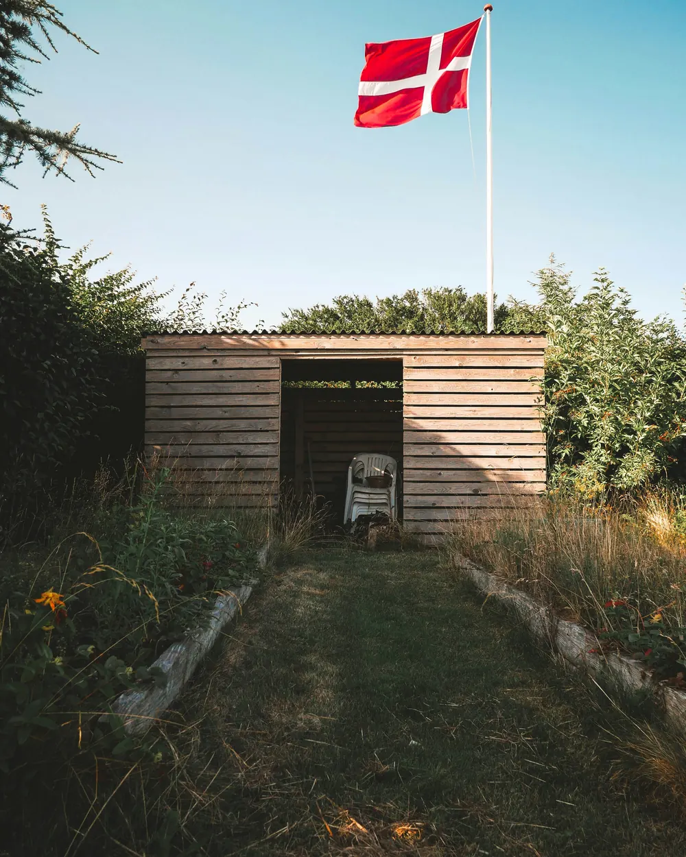 Dannebrog på en hvid flagstang bag et haveskur af træ