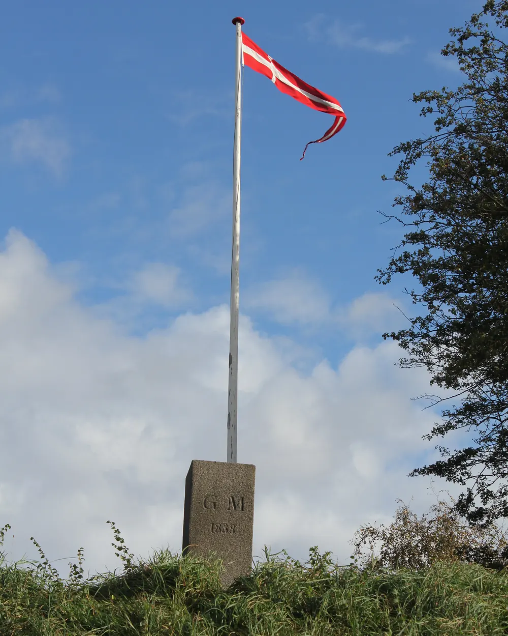 Flagstang med vimpel på en stenfod på en bevokset høj