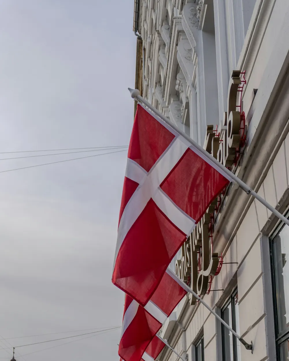 Dannebrog på korte flagstænger ud fra husfacader i en bygade